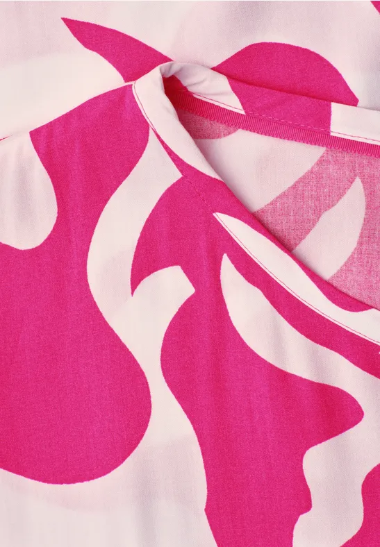 Knallpinke Bluse mit weißen, geschwungenen Mustern und dekorativem Knoten am Ausschnitt.