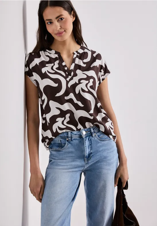 Vrouw met zwart-wit blouse, spijkerbroek en tas voor een lichte achtergrond.