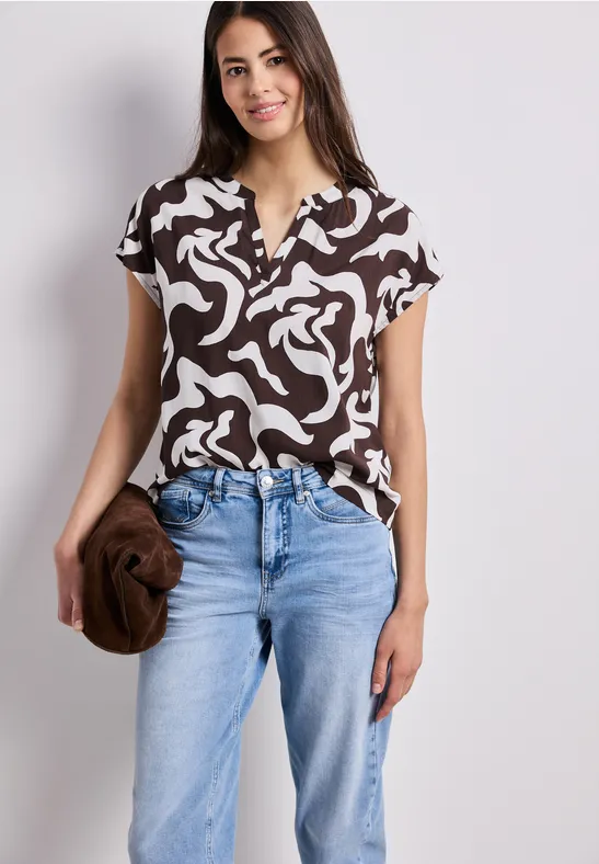 Vrouw draagt bruin-wit top met jeans, houdt een bruine clutch vast