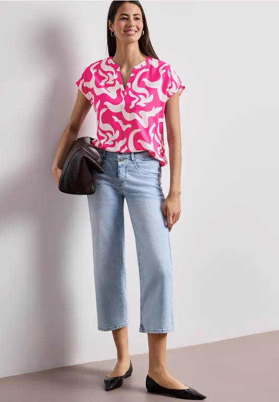 Vrouw in roze-wit patroon top, wijde lichtblauwe jeans, zwarte ballerina’s en een zwarte handtas