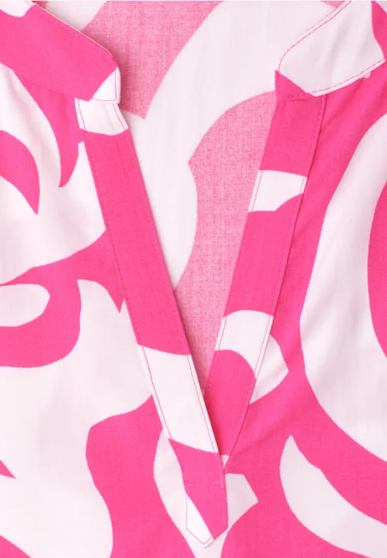 Close-up van een roze-witte top met abstract patroon en V-hals.