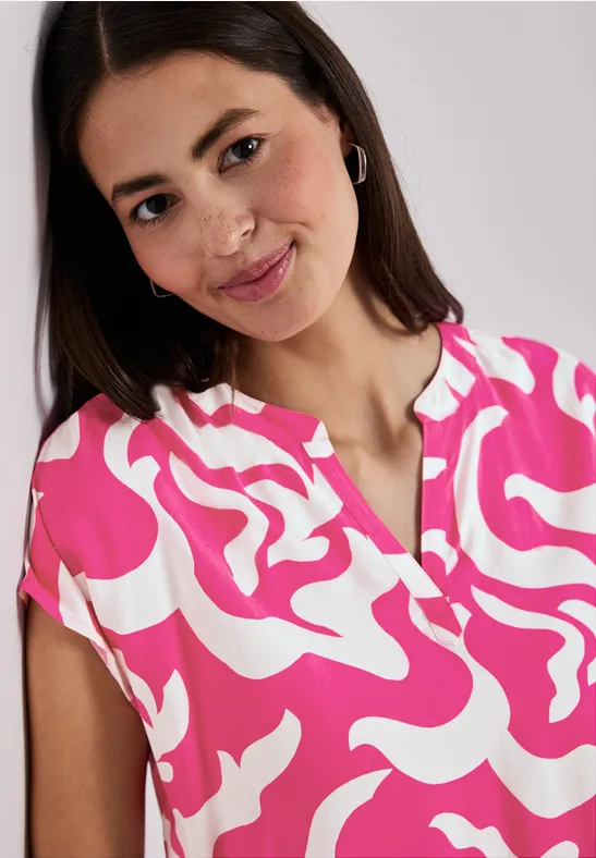 Vrouw draagt een roze-wit gebloemde top met korte mouwen en V-hals, haar aan één kant gestoken.