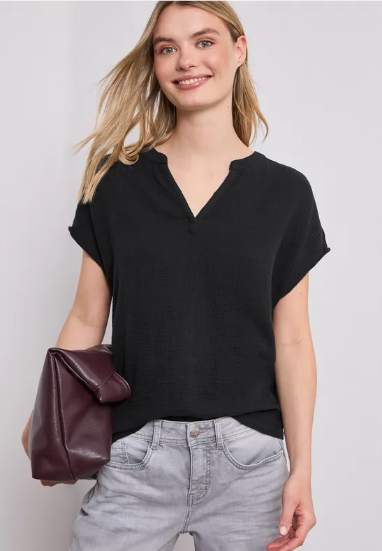 Vrouw met een zwarte blouse, grijze broek en een bordeauxrode tas in de hand.