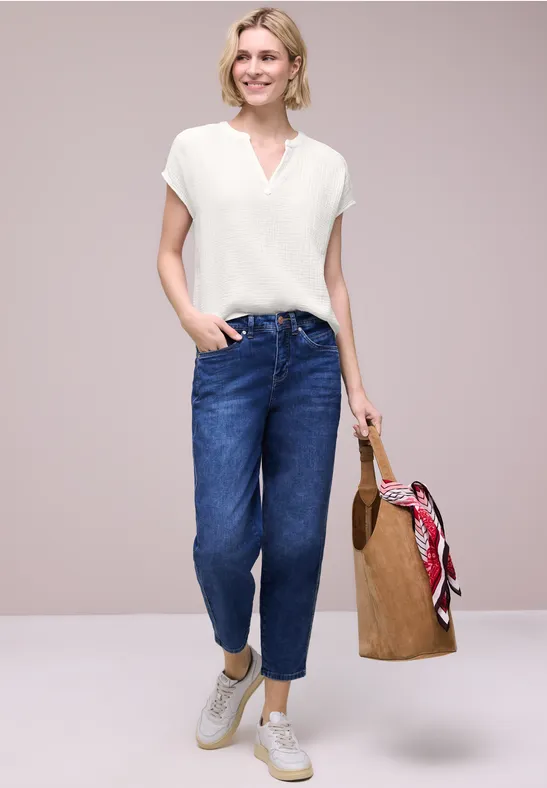 Vrouw met wit T-shirt, blauwe jeans, witte sneakers en rieten tas met rode sjaal.