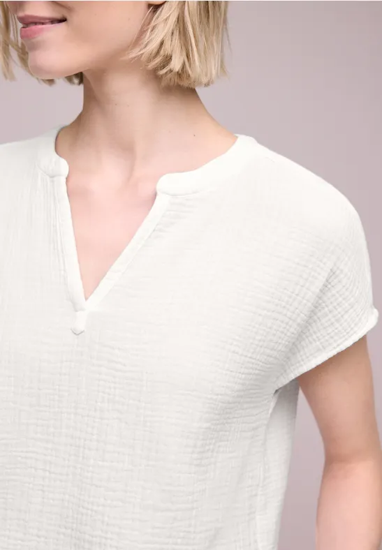 Een vrouw draagt een wit, gestructureerd T-shirt met korte mouwen en V-hals tegen een neutrale achtergrond.