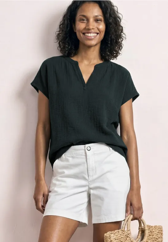 Vrouw in zwarte blouse en witte short met een strooien tas.