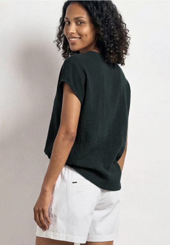 Persoon met krullend haar draagt zwart shirt en witte shorts, staat met de rug naar de camera, opzij gericht.