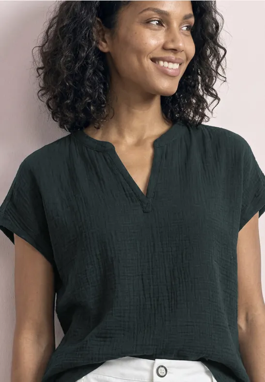 Een glimlachende vrouw met krullend haar draagt een zwarte blouse voor een roze muur.