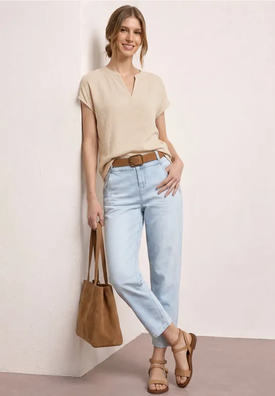 Vrouw in casual look met crèmekleurig shirt, lichtblauwe jeans, bruine riem, sandalen en bijpassende tas