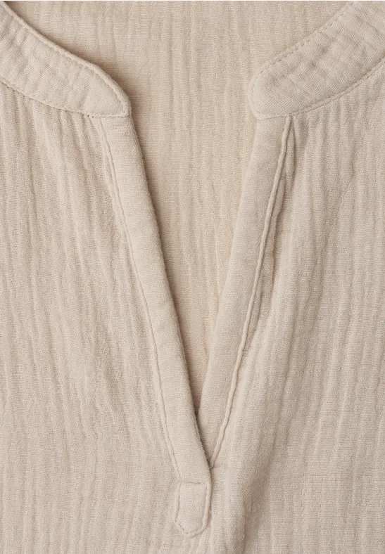 Close-up van een lichtbeige, geribbeld linnenstof met V-hals, vermoedelijk deel van een overhemd of jurk.