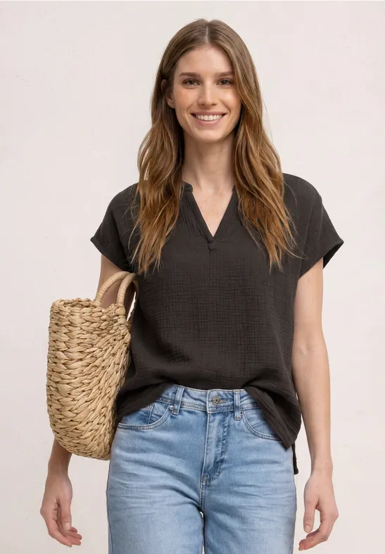 Femme en haut noir à manches courtes et jean bleu, portant un sac en paille tressée.