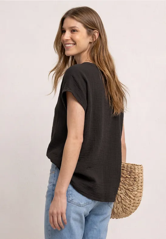 Femme portant un t-shirt noir et un jean bleu clair, vue de côté, avec un sac en paille.