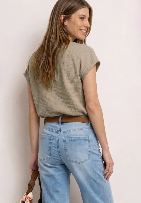 Achteraanzicht van een vrouw in een lichtblauwe jeans, kort shirt en bruine riem, met een tas in haar hand.