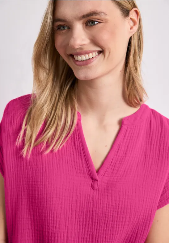 Frau trägt eine rosafarbene, texturierte Bluse mit V-Ausschnitt und kurzen Ärmeln.