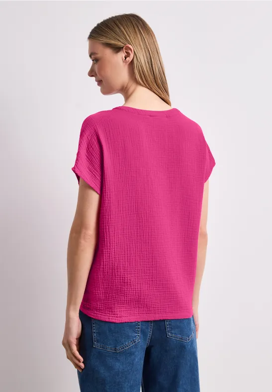 Eine Frau von hinten in pinkem Kurzarmshirt und blauen Jeans.