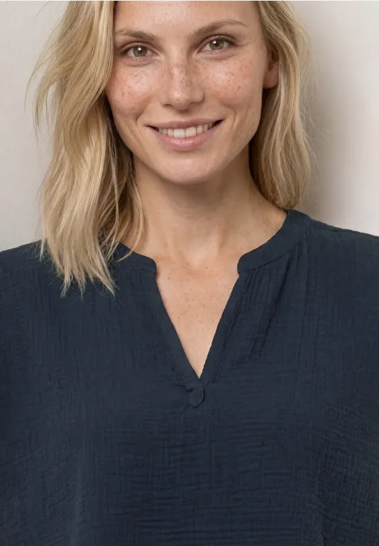 Oberkörper einer Person in dunkelblauem, luftigen Oberteil mit V-Ausschnitt und Knopfdetail.