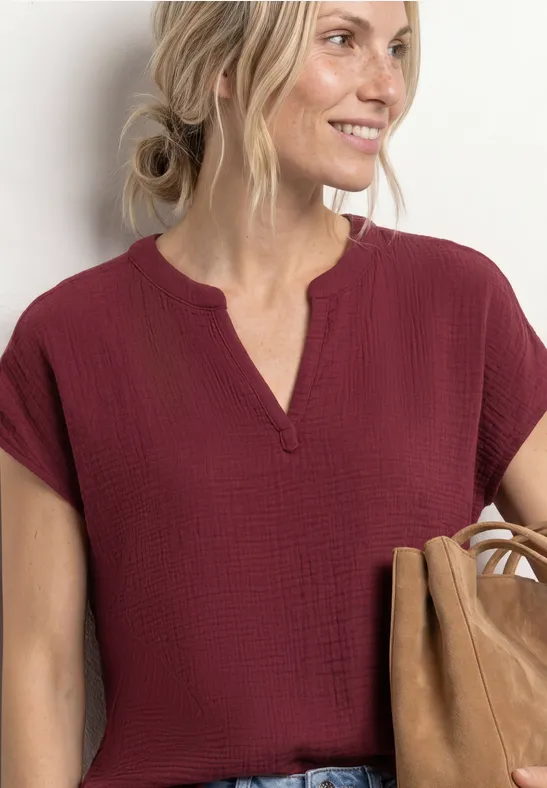 Frau in weinroter kurzärmeliger Bluse mit V-Ausschnitt hält eine braune Tasche