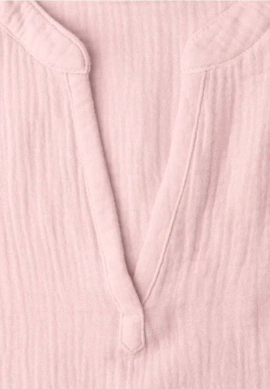 Close-up van een lichtroze bloes van luchtige stof met V-hals en decoratieve knoop.