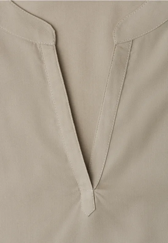 Nahaufnahme eines hellbeigen Baumwollshirts mit V-Ausschnitt und feiner Naht.