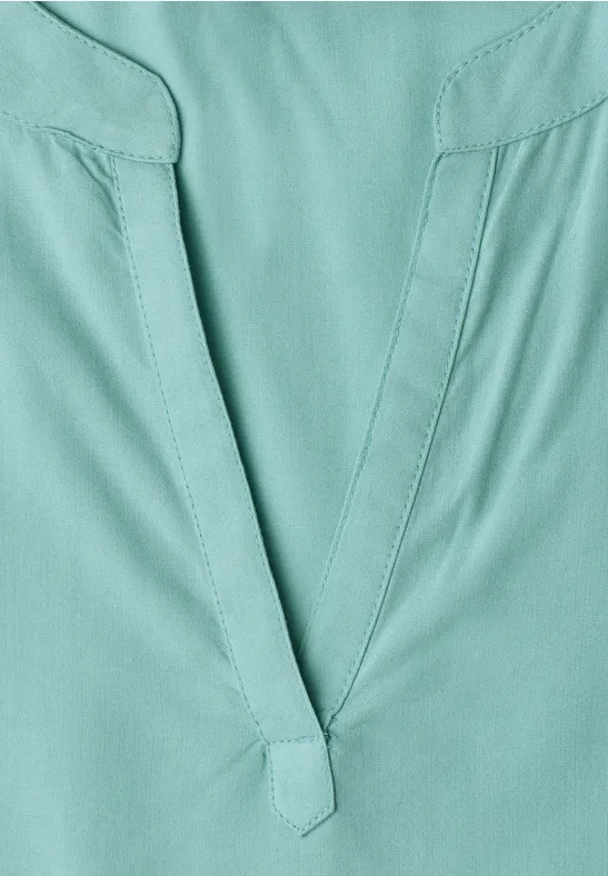 Gros plan d’un haut vert-bleu à encolure en V avec coutures apparentes.