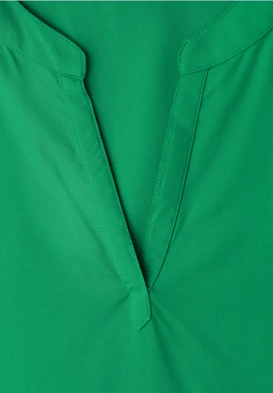 Nahaufnahme eines grünen V-Ausschnitt-Oberteils aus glattem Stoff.