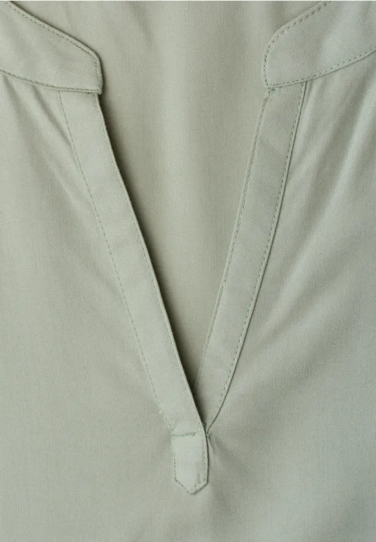 Nahaufnahme eines hellgrünen Kleidungsstücks mit V-förmigem Ausschnitt und minimalistischem Design.