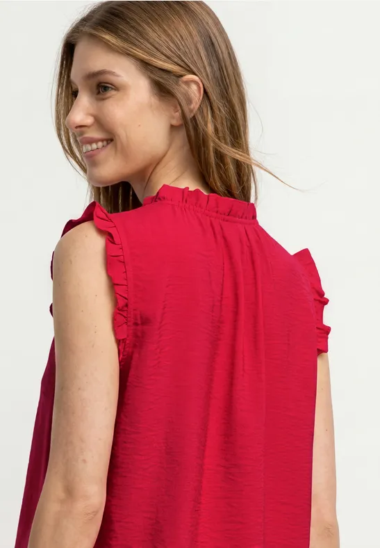 Ein Mädchen von hinten in rotem ärmellosem Kleid mit Rüschen an den Schultern.