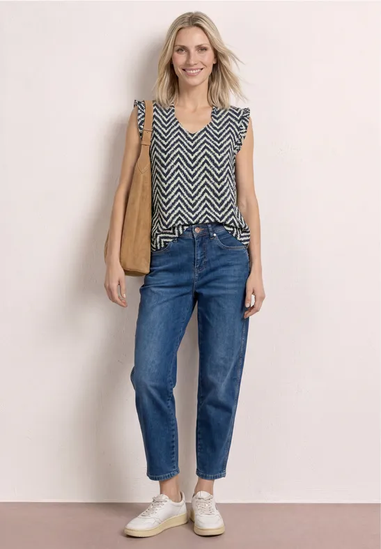 Frau in ärmellosem Zickzack-Top, Jeans, weiße Sneakers, braune Schultertasche