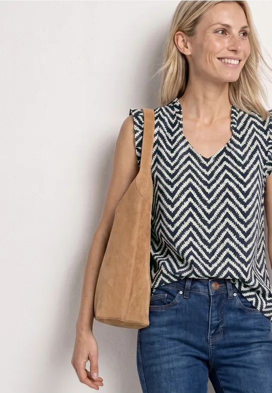 Frau in schwarz-weißem Zickzack-Top, Jeans und brauner Stofftasche