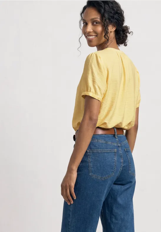 Frau trägt gelbes T-Shirt und blaue Jeans, Rückenansicht.
