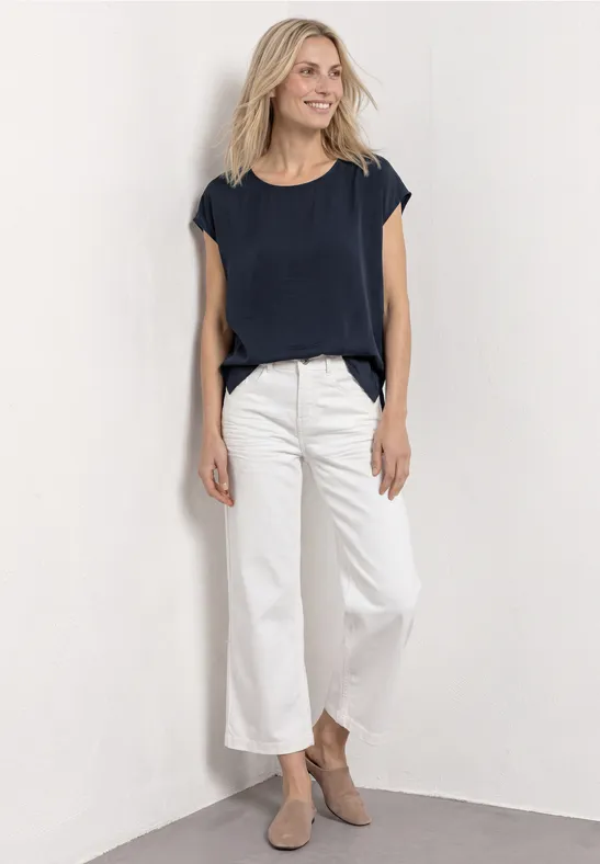 Frau trägt navy T-Shirt, weiße Culotte und beige Stiefeletten vor schlichtem Hintergrund.