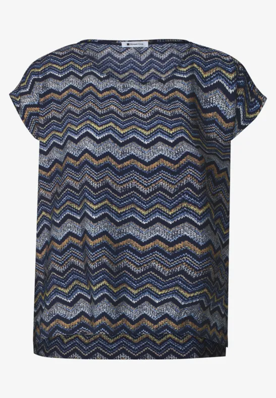 Kurze Damenbluse mit buntem Zickzackmuster in Blau, Senf und Weiß, rundem Ausschnitt und legerem Schnitt.