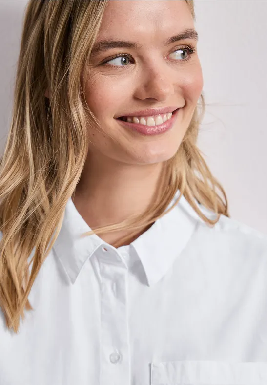 Vrouw in wit overhemd met ketting, gezicht vervaagd tegen lichte muur