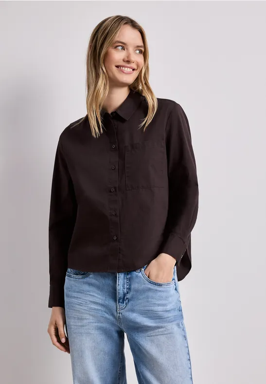 Femme portant une chemise noire et un jean bleu sur fond neutre.