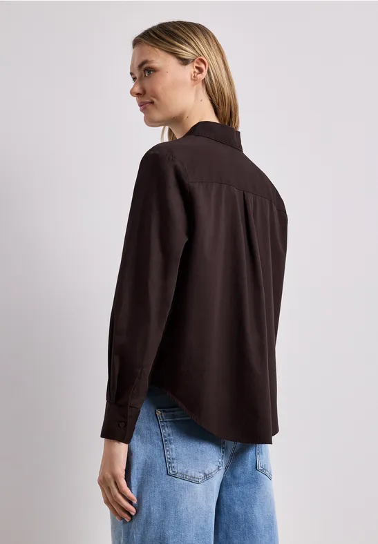 Femme de dos portant une chemise noire et un jean bleu sur fond clair.