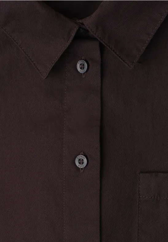 Chemise foncée avec col et patte de boutonnage; deux boutons et poche poitrine visibles.