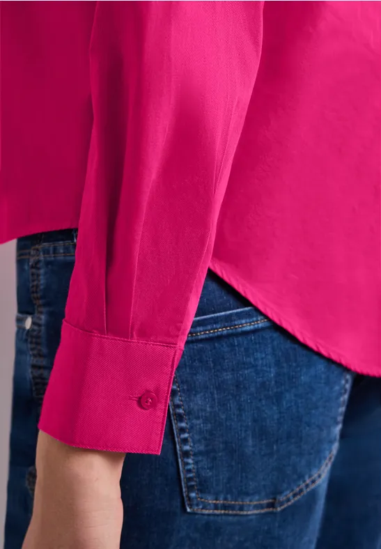 Seitliche Ansicht einer pinken Bluse über blauer Jeanshose.