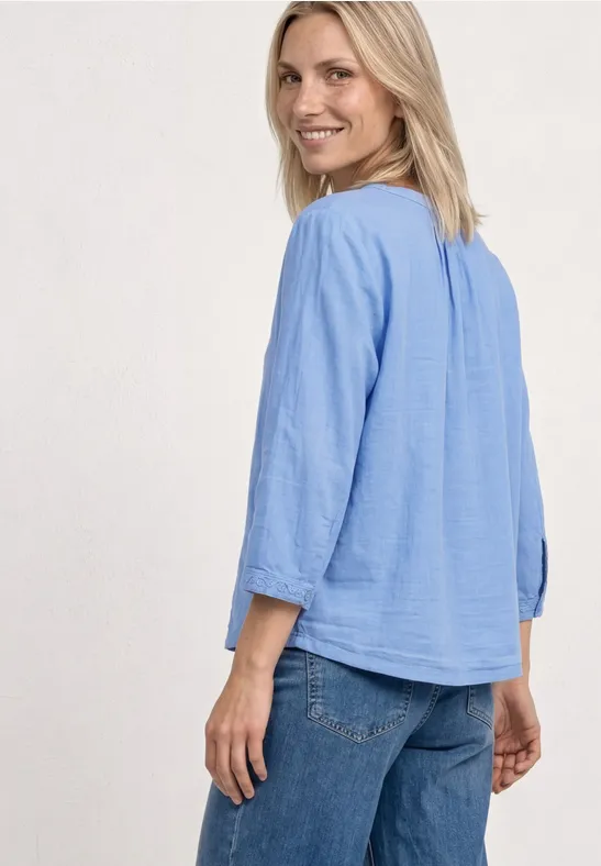 Kobieta od tyłu w jasnoniebieskiej luźnej bluzce 3/4 rękawach i dżinsach.