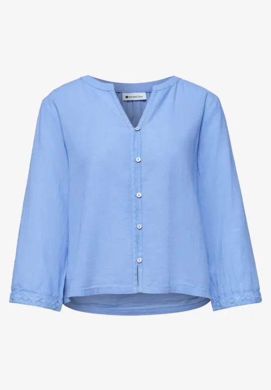 Jasnoniebieska bluzka z długimi rękawami, dekoltem w serek, zapięciem na guziki i lekko zaokrąglonym dołem.