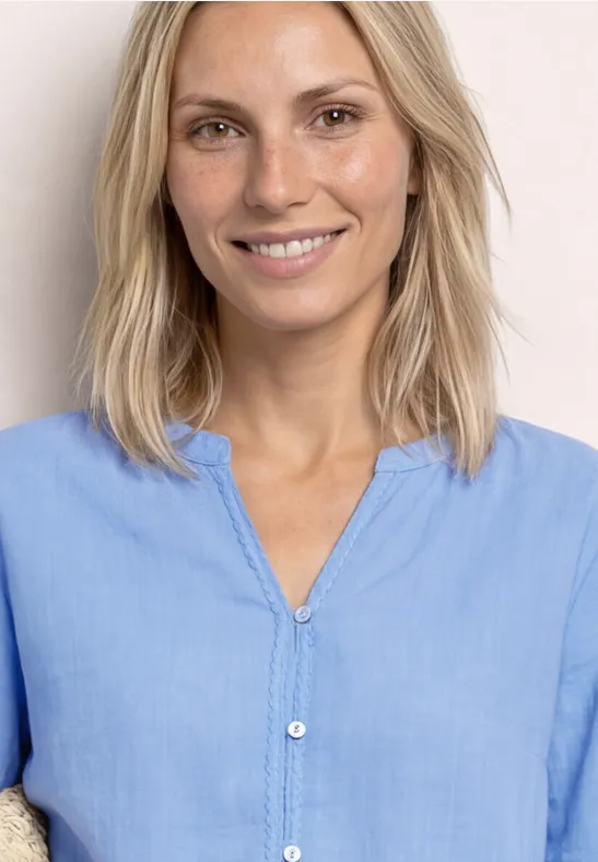 Kobieta z półdługimi blond włosami w jasnoniebieskiej koszuli na jasnym tle