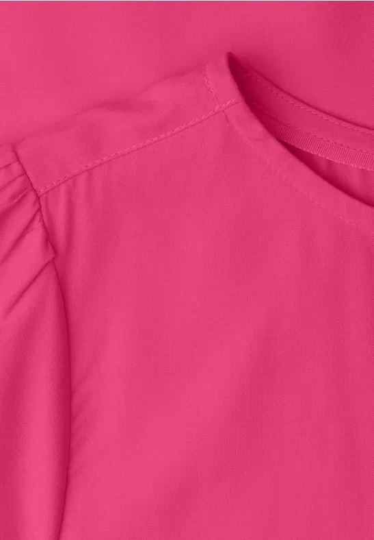 Nahaufnahme eines knallpinken Oberteils mit Rundhalsausschnitt und gerafftem Ärmel.