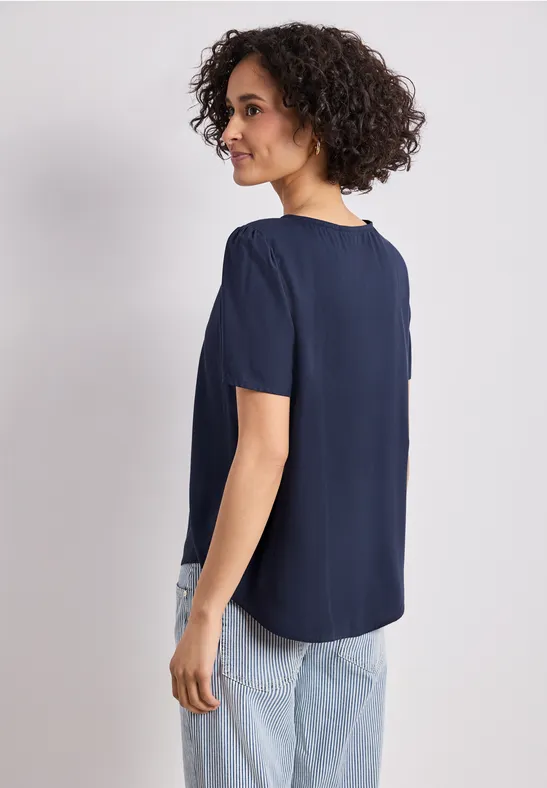 Vrouw van achter gezien in een donkerblauw shirt met korte mouwen en lichte jeans