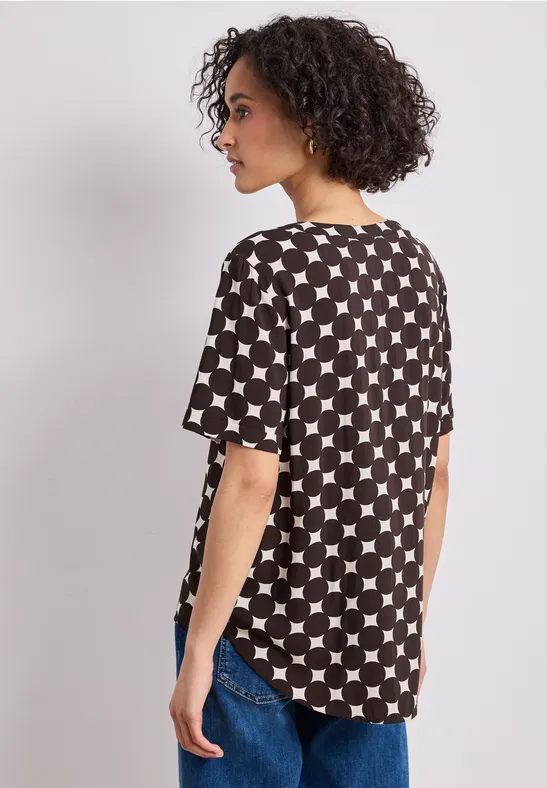 Frau mit lockigen Haaren trägt schwarzes T-Shirt mit weißem Sternenmuster und Jeans, von hinten fotografiert.