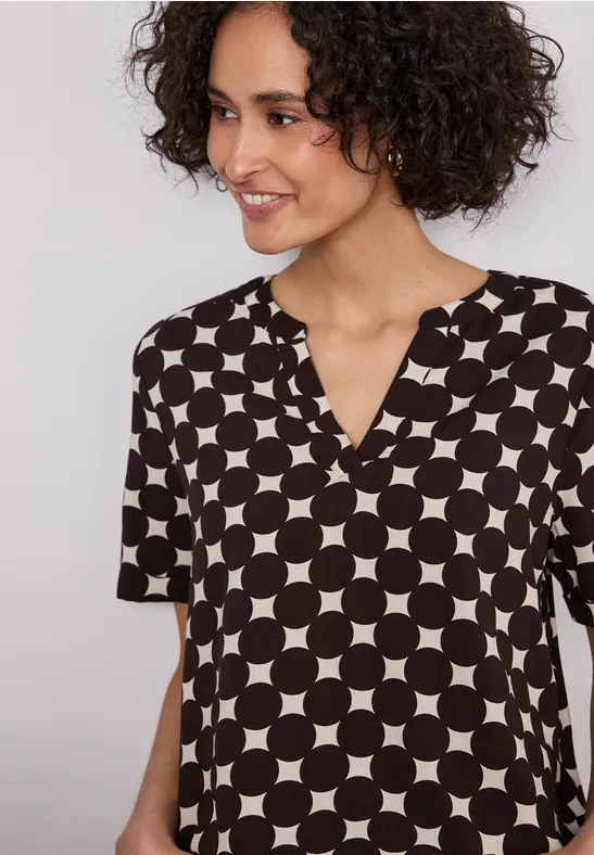 Eine Person trägt eine kurzärmelige Bluse mit schwarzem Hintergrund und weißem Kreismuster.