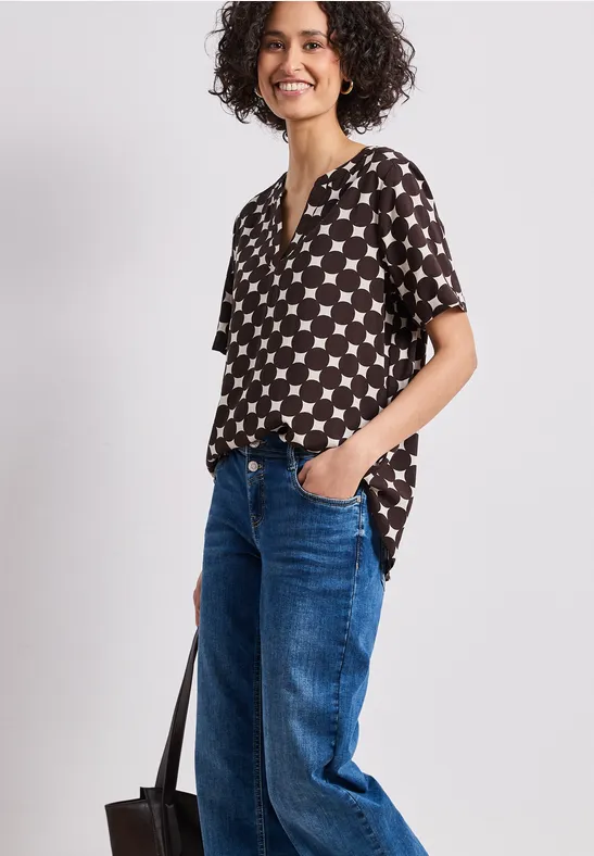 Person trägt schwarzes Shirt mit weißen Sternen, blaue Jeans und schwarze Tasche.