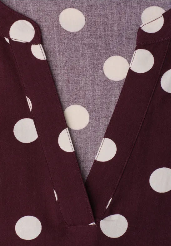 Gros plan d’un haut col V bordeaux à pois blancs.