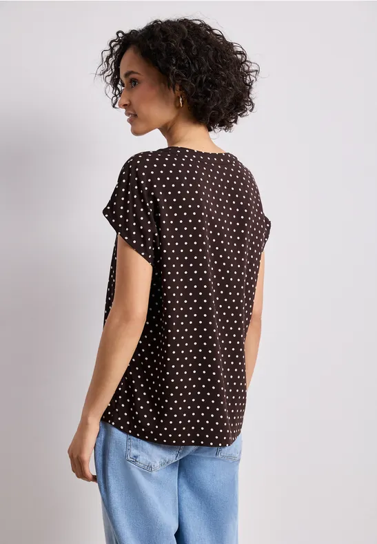 Vue de dos d'une personne portant un t-shirt noir à pois blancs et un jean bleu