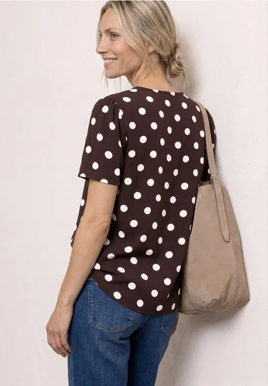 Femme vue de dos portant un haut marron à pois, un jean bleu et un sac en toile beige.