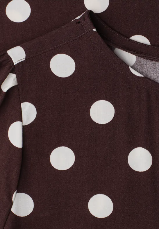 Tissu marron à gros pois blancs avec couture apparente, semblant appartenir à un vêtement avec poche.