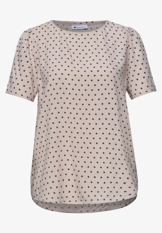 Beige T-shirt met zwarte polkadots en korte mouwen.